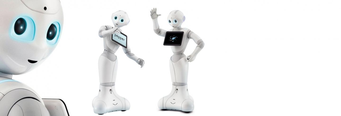 Drie witte robots met blauwe ogen genaamd Pepper, zij hebben een iPad voorop voor informatie op te lezen.