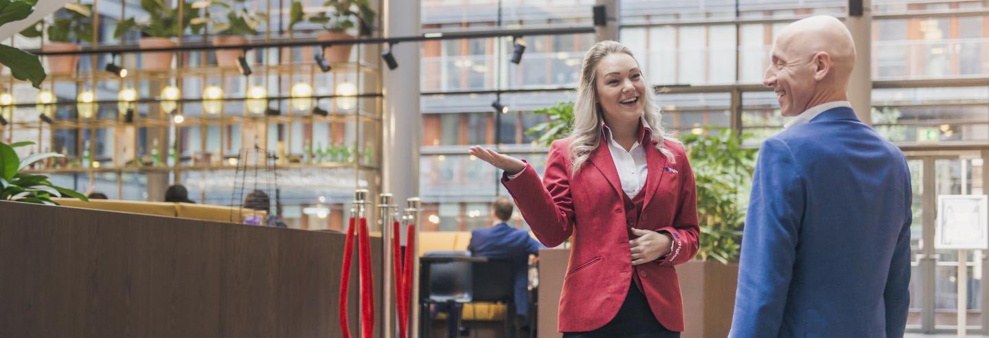 Gastvrouw in uniform wijst mannelijke bezoeker de weg.