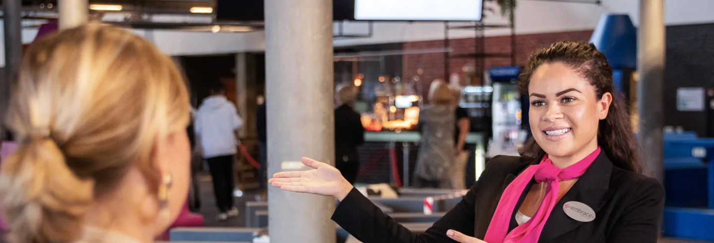 Medewerkster van Embrace wijst vrouwelijke bezoeker de weg.