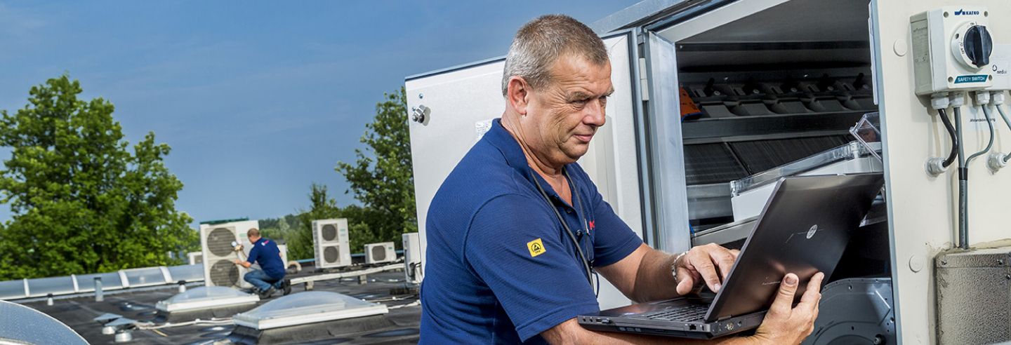 Man aan het werk met zijn laptop bij een ventilatie installatie op het dak.