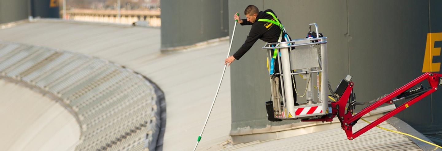 een medewerker van Degenaar is in een bakje van een hoogwerker met een telescoopstok het dak aan het schoonmaken