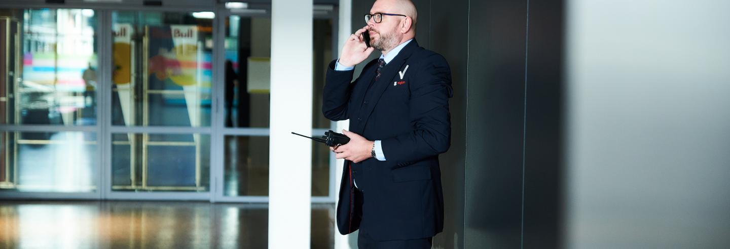 Mannelijke beveiliger loopt in uniform rond en praat in een telefoon.