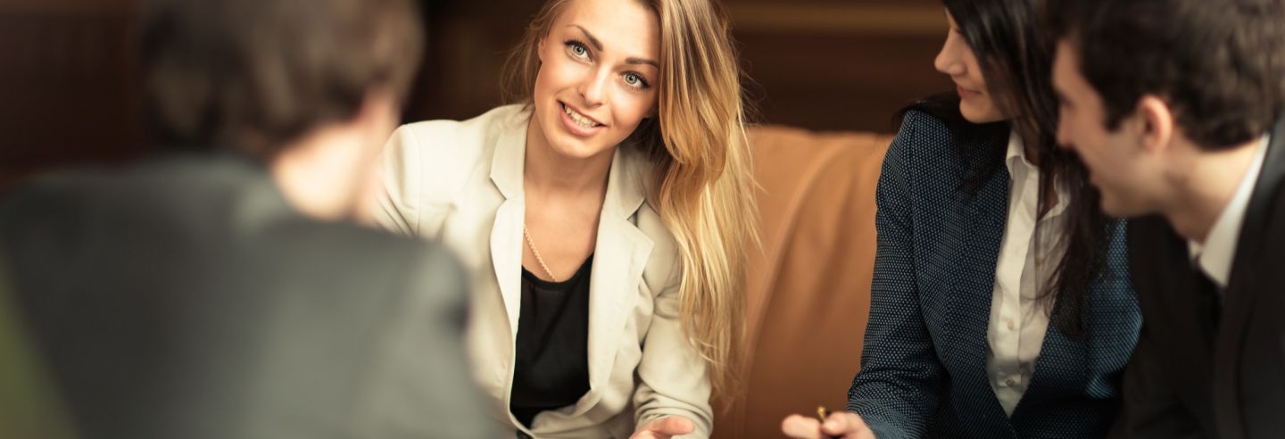 Een viertal collega's die in een informele zetting (bank en lage tafel) met elkaar in overleg zijn.