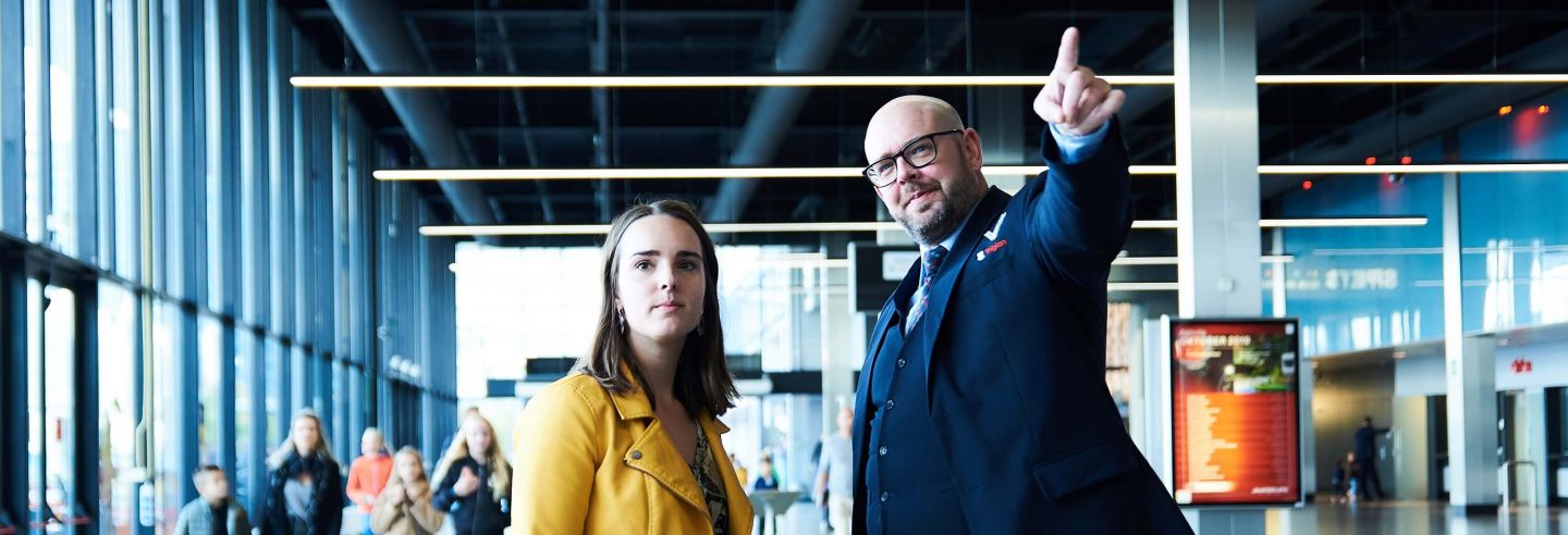 Mannelijke beveiliger in uniform wijst aan een vrouwelijke voorbijganger de weg op Jaarbeurs Utrecht.