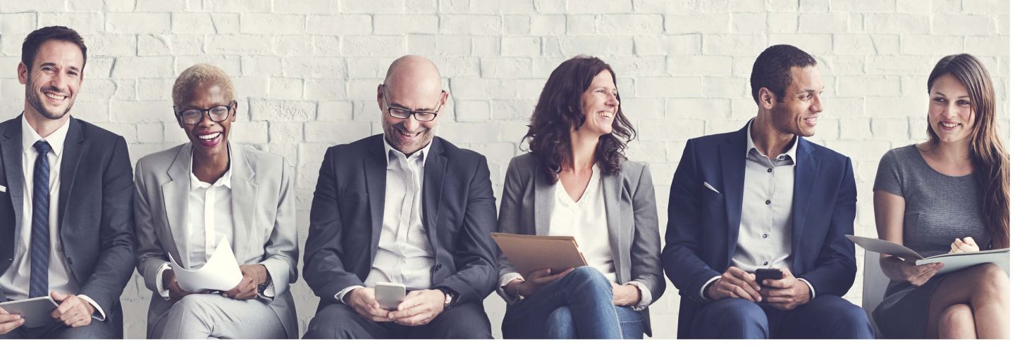 Groep interimmanagers zittend op een rij voor een muur vrolijk lachend en met elkaar in gesprek