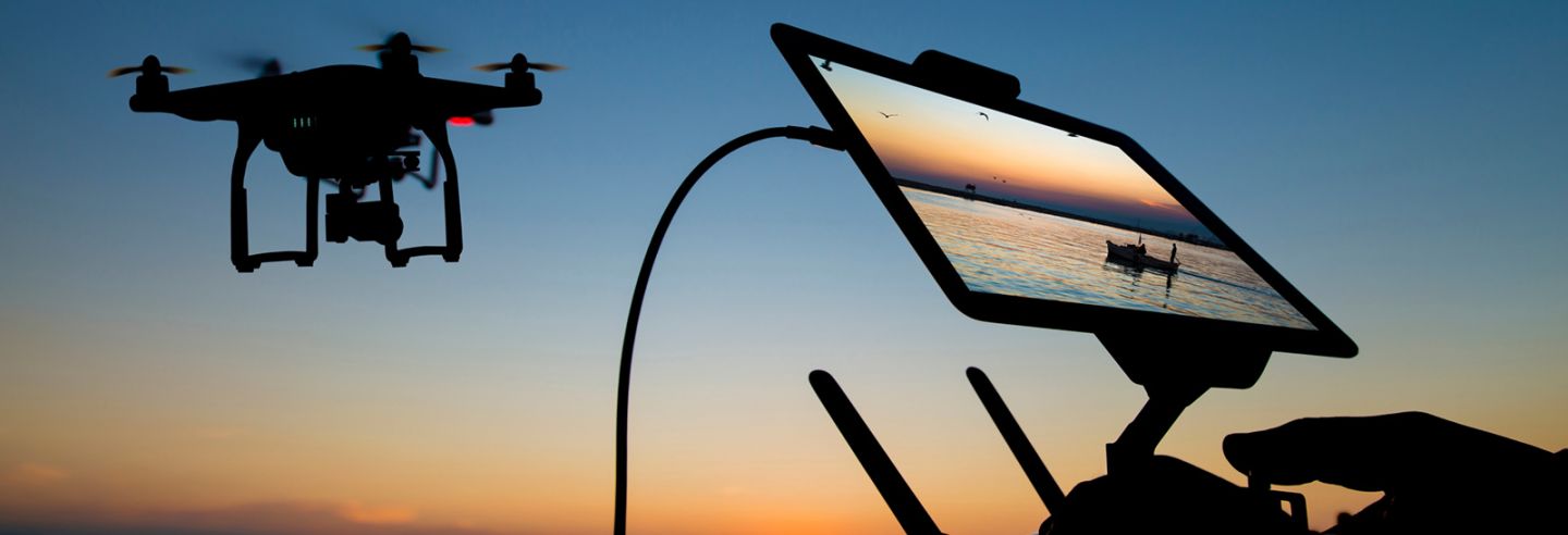Bij zonsondergang wordt een drone bestuurd door een persoon die de beelden ziet op een schermpje.