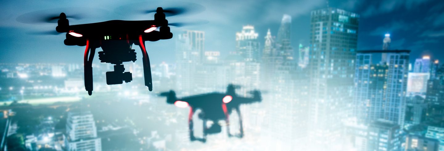 Twee drones die in de avond vliegen over een complex.