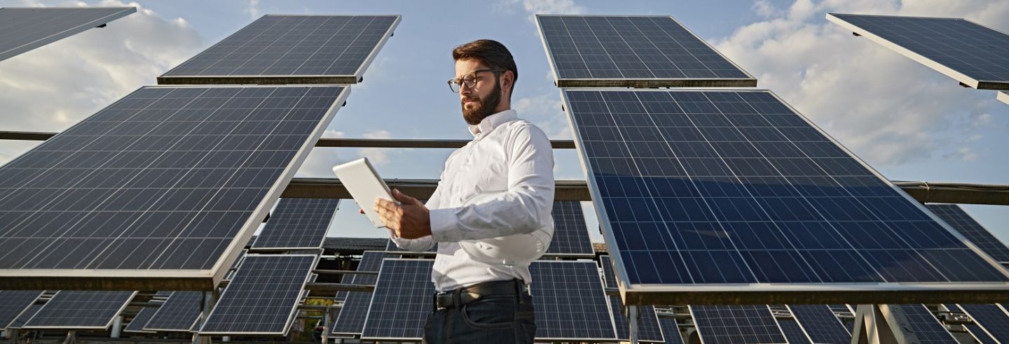 Medewerker energiemanagement analyseert data op tablet staand naast veld met zonnepanelen