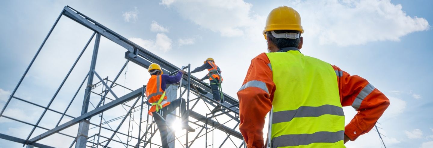 Opzichter kijkt op bouwplaats naar collega's die aan het werk zijn op een steiger.