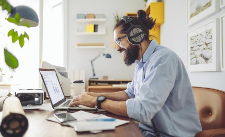 thuiswerk Een man met baard en koptelefoon op zijn oren aan het werk achter een laptop