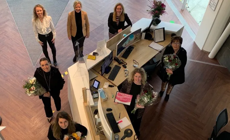 Zeven vrouwen staan geposeerd bij de receptie van Ingenico. Hierbij wordt de foto van bovenaf genomen en staan zij op anderhalve meter afstand van elkaar.