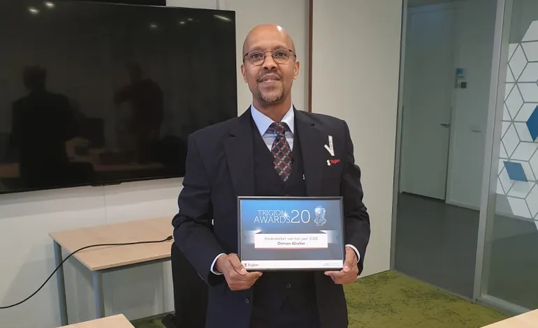 Mannelijke beveiliger in uniform staat geposeerd voor de camera en heeft zijn certificaat en voucher in handen.