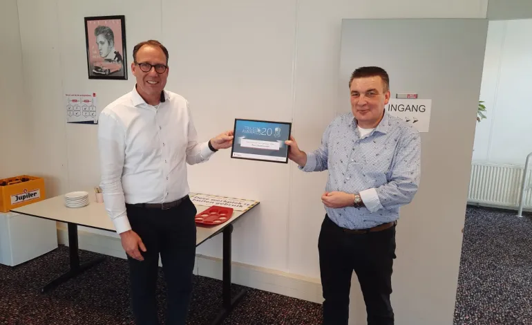 Twee mannen staan geposeerd voor de camera waarbij de regiodirecteur het certificaat overhandigd aan de collega beveiliger.