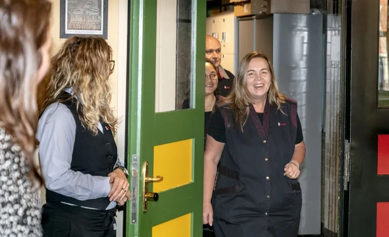 een schoonmaakmedewerker van de Hanzehogeschool wordt lachend opgewacht door haar collega's terwijl ze de deur doorloopt