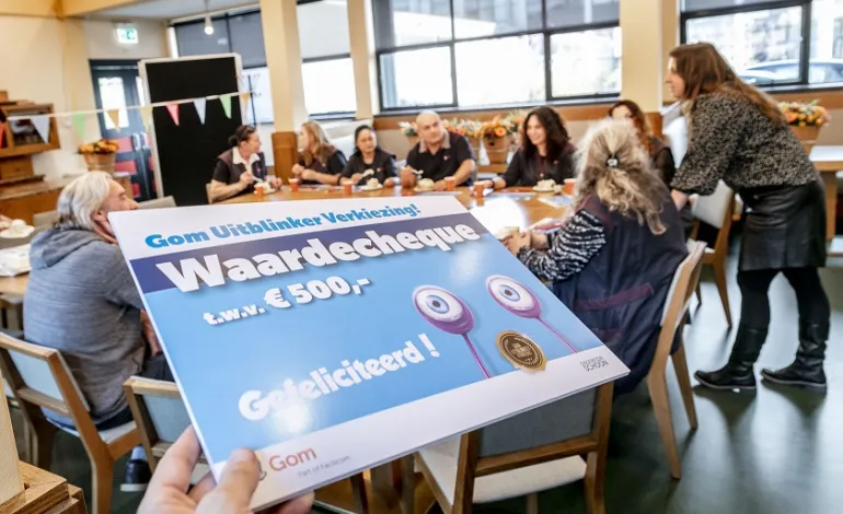 het complete schoonmaakteam van de Hanzehogeschool zit bijeen aan tafel, op de voorgrond wordt de waardencheque voor de Gom Uitblinker getoond