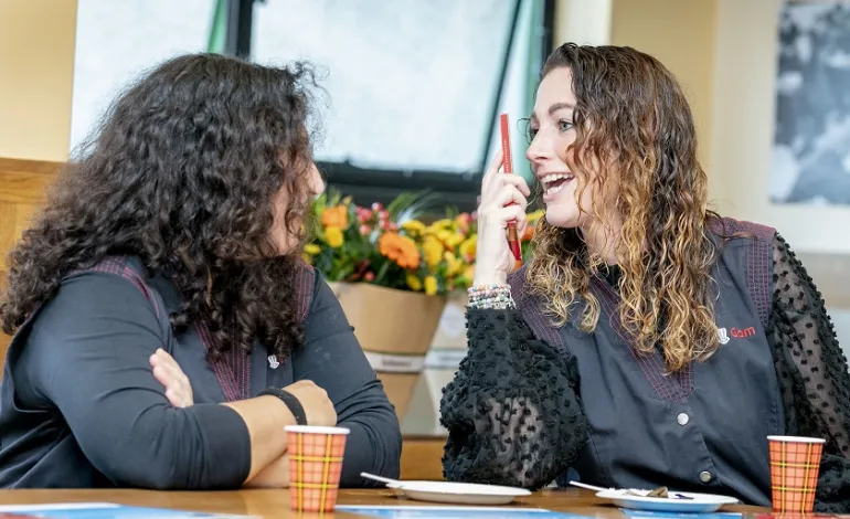 2 schoonmaakmedewerkers zitten aan tafel en praten lachend met elkaar