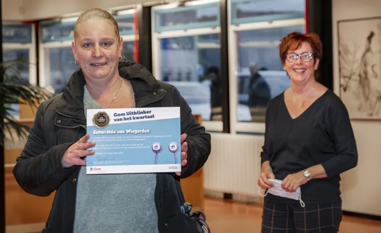 Esmeralda van Wingerden houdt lachend haar oorkonde voor de Gom Uitblinker vast, met op de achtergrond haar leidinggevende