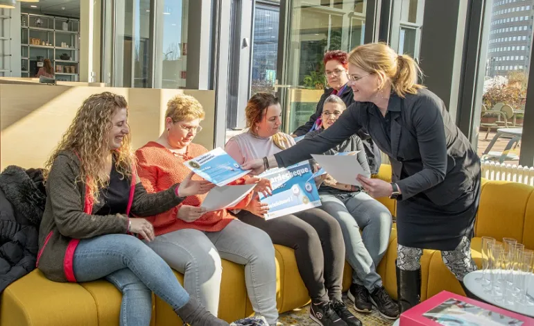 5-tal schoonmaakmedewerkers krijgen van hun leidinggevende hun oorkonde uitgedeeld terwijl ze op een rijtje op een bank zitten