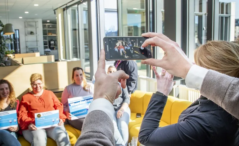 5-tal schoonmaakmedewerkers zitten met hun oorkonde op de bank en er worden foto's van hen genomen met telefoons