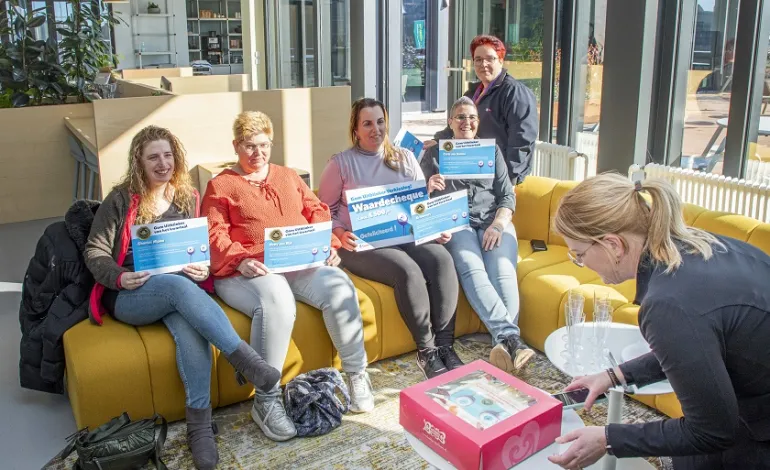 5-tal schoonmaakmedewerkers zitten met hun oorkonde op de bank terwijl de taart aangesneden gaat worden