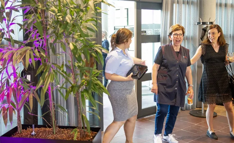 Schoonmaakster Ajsa en aan weerszijde van haar 2 leidinggevenden lopen een ruimte binnen