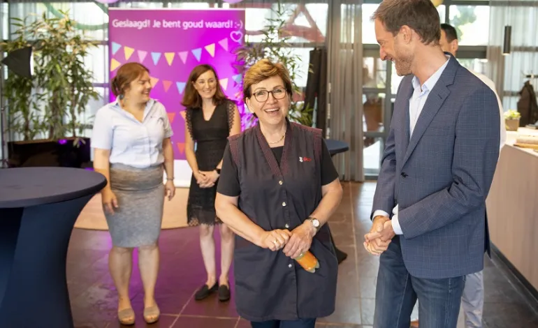 Schoonmaakster Ajsa kijkt lachend de camera in terwijl Jeroen Hofmeester haar lachend aankijkt terwijl hij naast haar staat