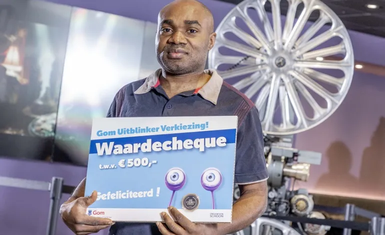 schoonmaakmedewerker Godday Peter staat met een waardecheque in zijn handen voor een filmprojector