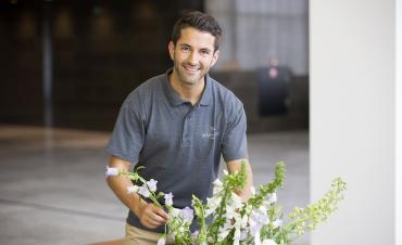 Een medewerker van Magnifique, gekleed in een polo, is een bos bloemen aan het schikken