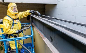 een medewerker van Gom Specialistische reiniging in een geel en geheel afgesloten beschermend pak zuigt gevaarlijke stoffen op.