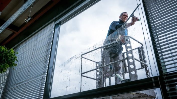 een glazenwasser van Gom Specialistische Reiniging van binnenuit gezien in een hoogwerkerbakje, die de ramen zeemt