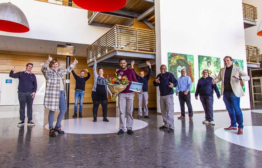 een groep van 8 collega's van Gom Offices staan juichend om Gom Uitblinker Edman Janga die een bos bloemen en een waardencheque in zijn handen heeft