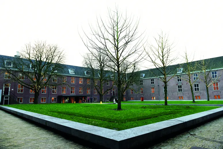 Dit is de binnentuin van de Hermitage in Amsterdam met een groot groen grasveld met verschillende grote bomen.