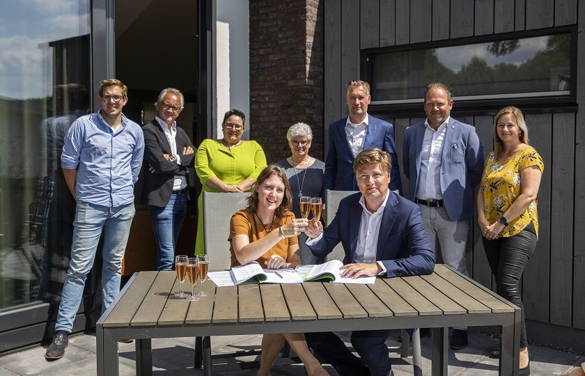 7 personen staan achter 2 personen die klinken met champagne na het ondertekenen van het contract tussen Landal en Gom Hospitality