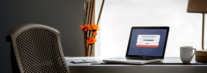 Foto van een laptop (macbook) op een bureau, naast een bloemetje en een lapm