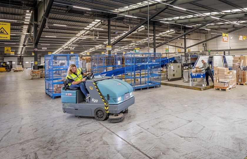 een medewerker van Gom Logistiek zit op een schrobzuigmachine en schrobt de vloer in de bedrijfshal