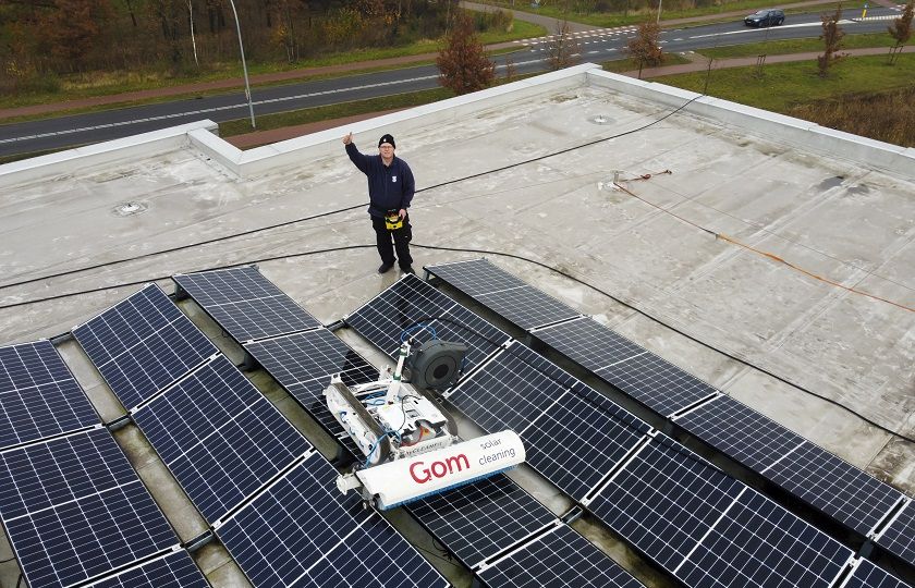 Sander Henten zwaait lachend in de camera terwijl hij op een dak met behulp van de solar max zonnepanelen reinigt.