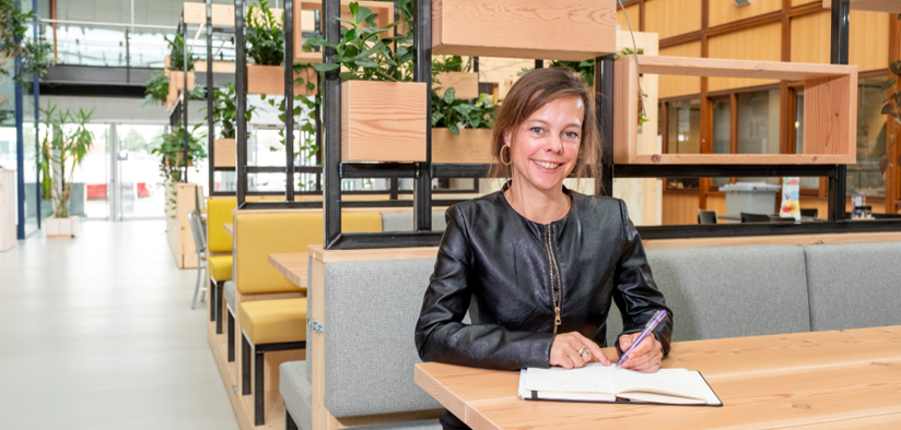 Juliette Sprangers aan een bureau in een openbare ruimte terwijl zie schrijft in een notebook.