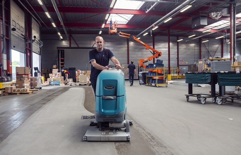 een medewerker van Gom Logistiek loopt achter een schrobzuigmachine en maakt hiermee de vloer van een distributiecentrum schoon