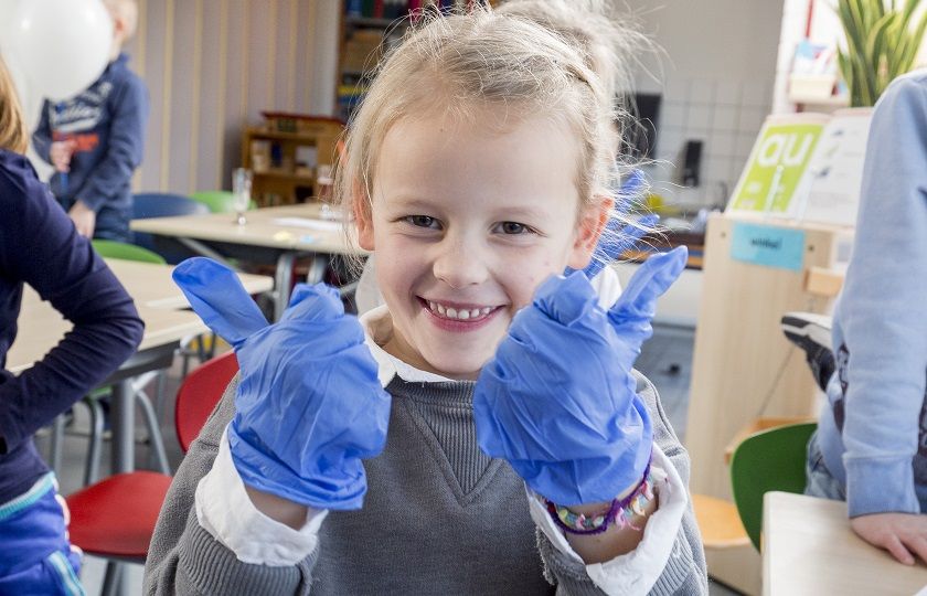 Een leerling van een basisschool met schoonmaakhandschoenen aan steekt beide duimen omhoog