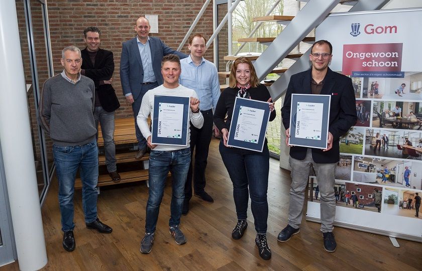 3 medewerkers van Gom Logistiek staan lachend met hun diploma van de opleiding Basis Veiligheidskunde in hun hand, hun leidinggevenden plus de docent staan lachend om hen heen