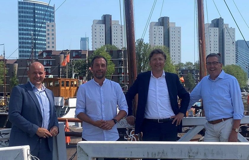 Vier mannen kijken lachend in de camera met de skyline van Rotterdam achter zich