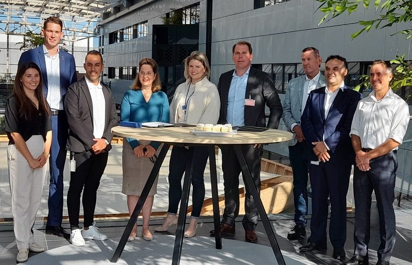 Een groep van 9 mensen staan om een tafel en kijken in de camera.