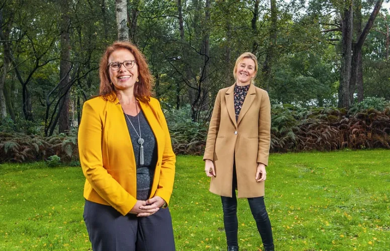 Twee dames staand op een grasveld kijken lachend in de lens