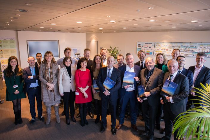 Een groep mannen en vrouwen in zakelijke kleding staan geposeerd in een zaal op Schiphol Amsterdam met een certificaat in hand.