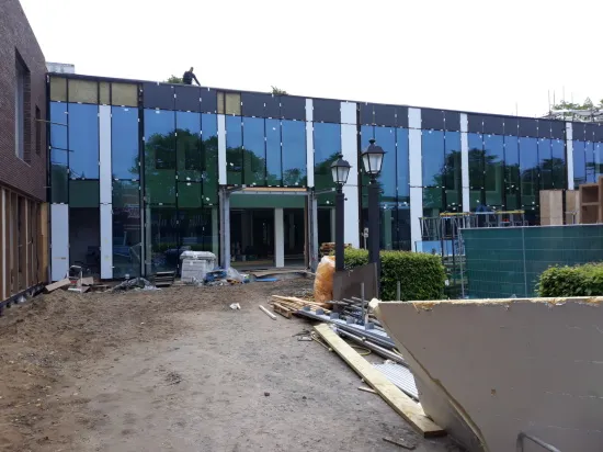 Foto van het gemeentehuis in Putten tijdens de renovatie, met bouwmaterialen en een deels afgewerkte glazen gevel.