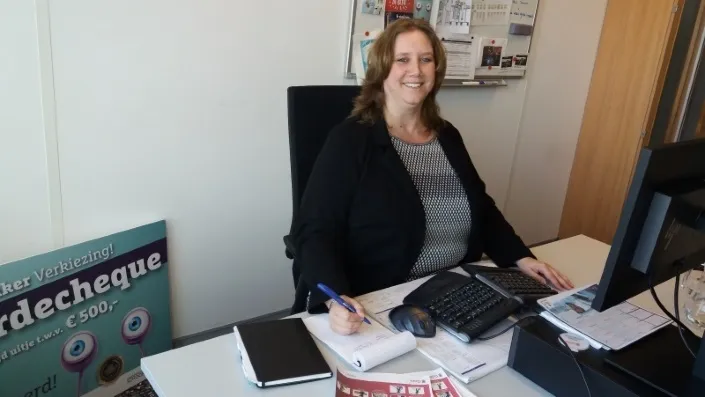 Barbara van der Kooij, communicatiemedewerker bij Gom, lachend achter haar bureau terwijl ze aantekeningen maakt op kantoor.