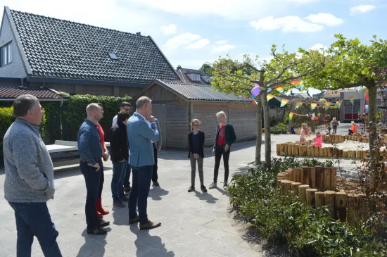 Bezoekers en schoolvertegenwoordigers bekijken het vernieuwde schoolplein van basisschool De Hoeksteen in Heerenveen, ingericht voor natuurlijk spelen met groen en houten speelplekken.