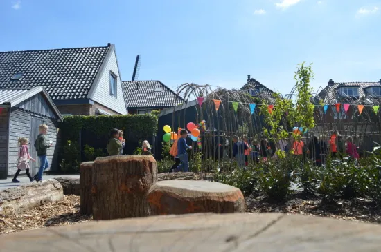 Kinderen spelen op het vernieuwde schoolplein met boomstammen, een wilgentunnel en vrolijke versiering tijdens de opening van het project Natuurlijk Spelen.