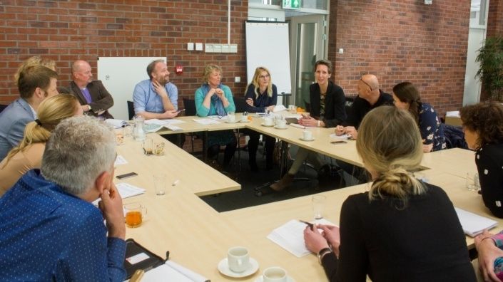 een grote groep van ruim 13 personen zit rondom een vergadertafel