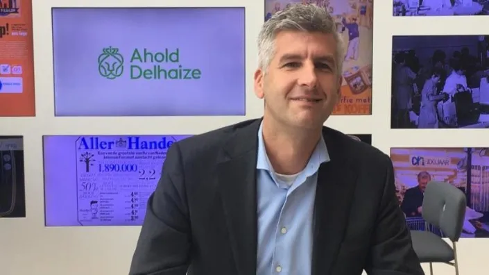 Michiel Kooijman, implementatiemanager bij Gom, zit aan tafel in een ruimte met Ahold Delhaize-logo op de achtergrond tijdens een gesprek over facilitaire samenwerking.